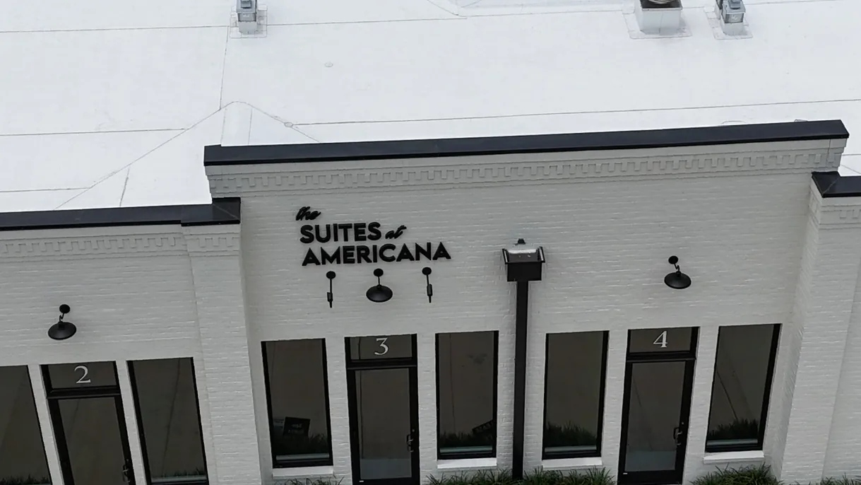 Aerial front view showing a clean, white commercial TPO flat roof replacement on a multi-suite commercial retail facility in Baton Rouge, Louisiana.