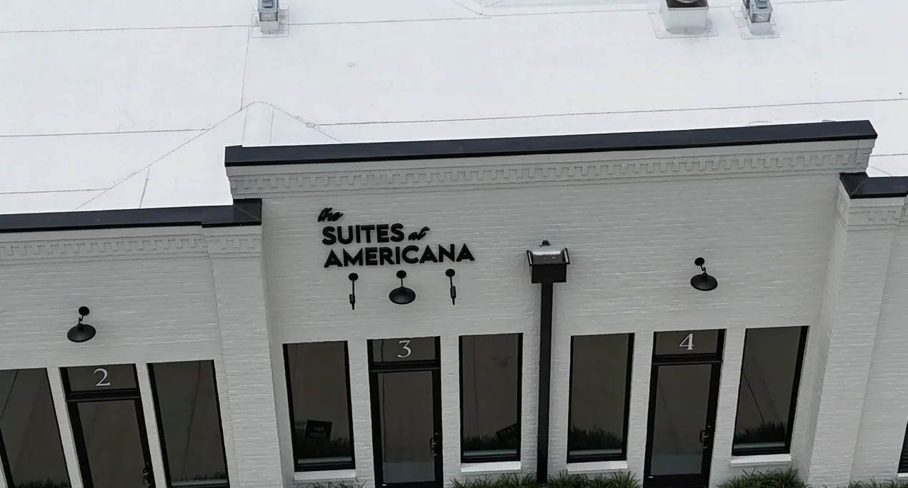 Aerial front view showing a clean, white commercial TPO flat roof replacement on a multi-suite commercial retail facility in Baton Rouge, Louisiana.
