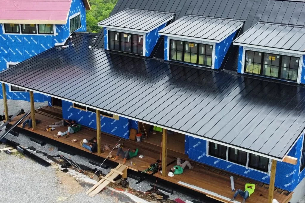 Wide elevated shot of roofing contractors installing custom black standing seam metal roof panels on a luxury home in Louisiana.